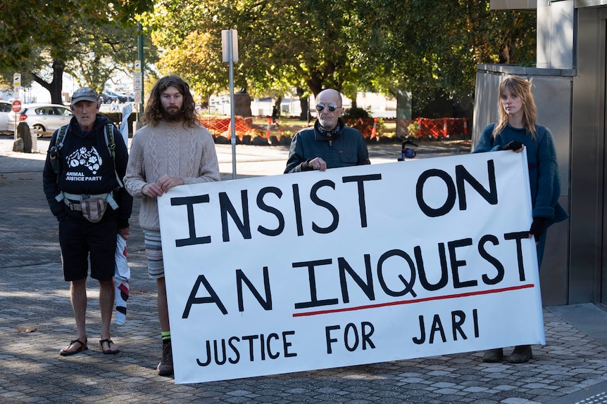 Campaigners hold up a sign saying 'Insist on an inquest. Justice for Jari' outside a court building.