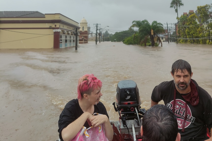 Woman with pink hair and man on boat surrounded by floodwater as high as telephone lines