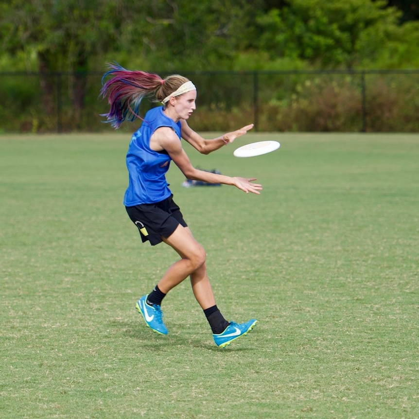 Girl with bright pink, blue and purple hair catches a frisbee