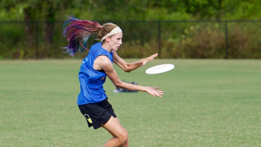 Girl with bright pink, blue and purple hair catches a frisbee