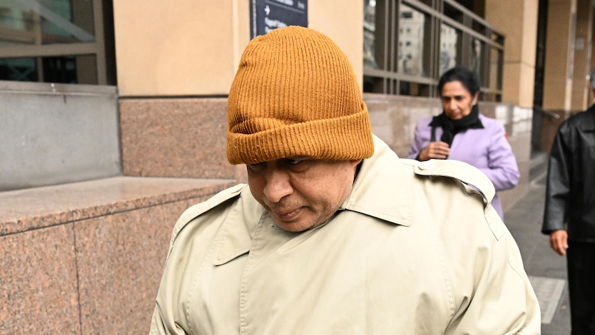 Naotunne Vijitha, dressed in an overcoat and yellow beanie, walks outside a court building in Melbourne.