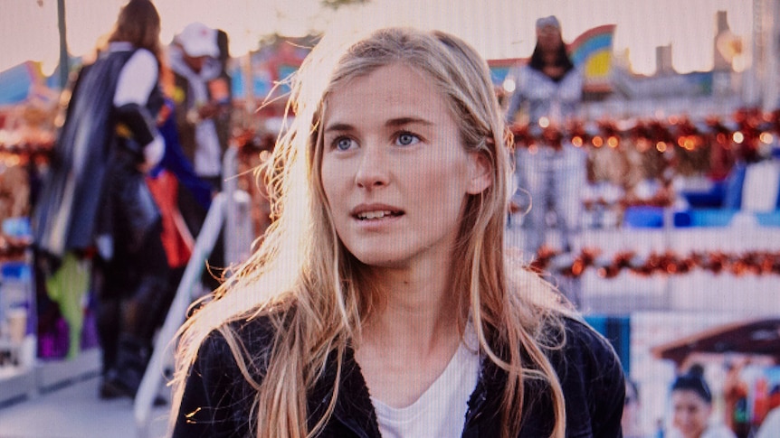 Photograph of Alex The Astronaut standing at a carnival with rides in the background