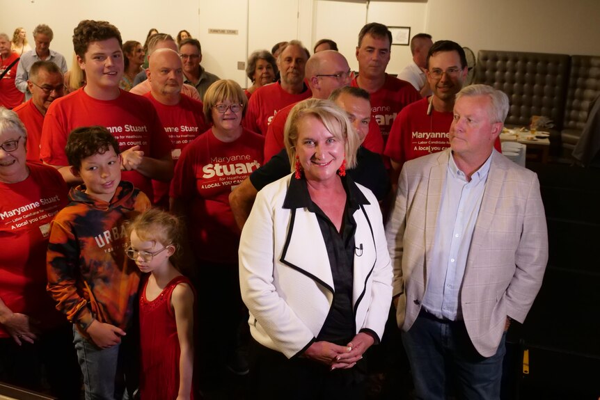 Smiling woman in white jacket surrounded by people wearing red shirts