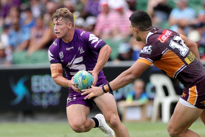 Melbourne Storm's Harry Grant looks to pass the ball while playing Brisbane Broncos' David Fifita tries to tackle him.