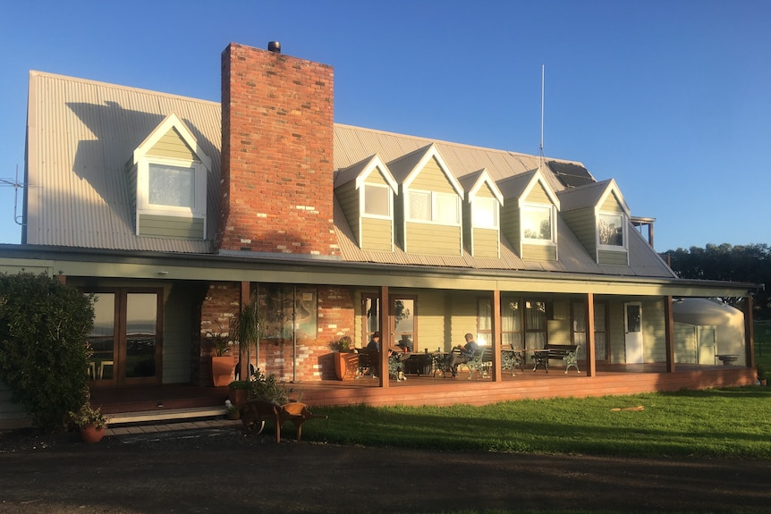 Two story eco lodge with large green lawns and people sat on the veranda