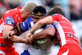 A Canterbury Bulldogs NRL player carries the ball as he is tackled by two St George Illawarra opponents.