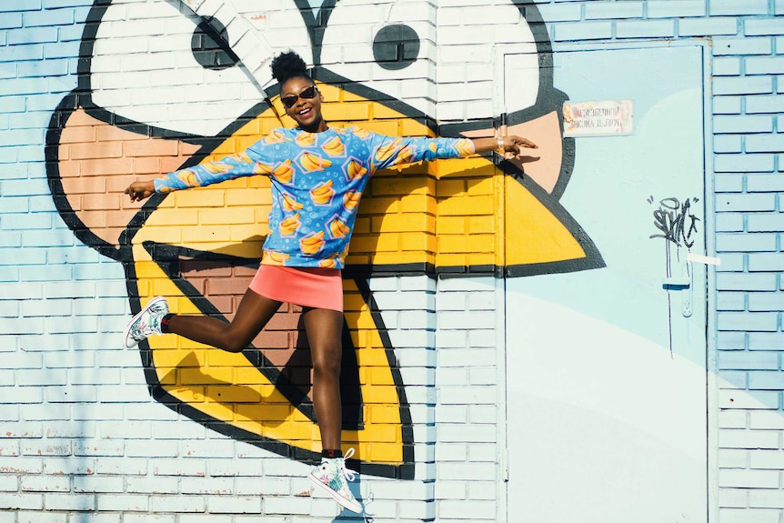 Woman jumping mid-air in front of a wall with graffiti to depict the freedom of leaving work with all your tasks complete.