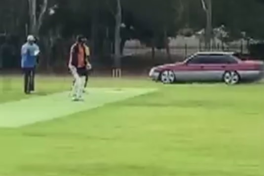 A car next to a cricket pitch.