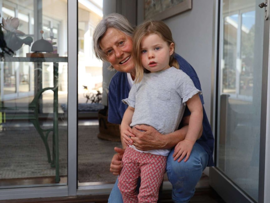 A woman with grey hair holds a child standing in front of an open door