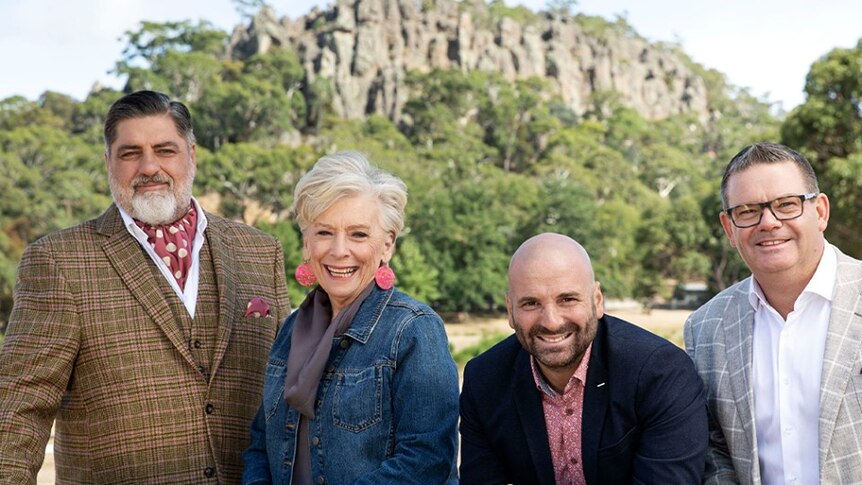 Matt Preston, Maggie Beer, George Calombaris and Gary Mehigan, left to right, stand in front of a cliff face with trees in back.