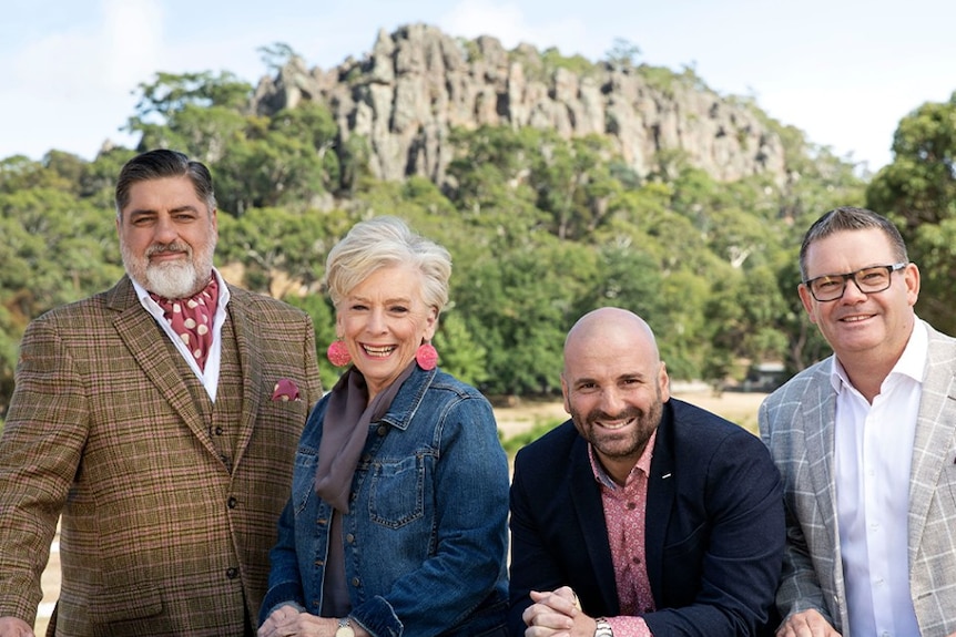 Matt Preston, Maggie Beer, George Calombaris and Gary Mehigan, left to right, stand in front of a cliff face with trees in back.