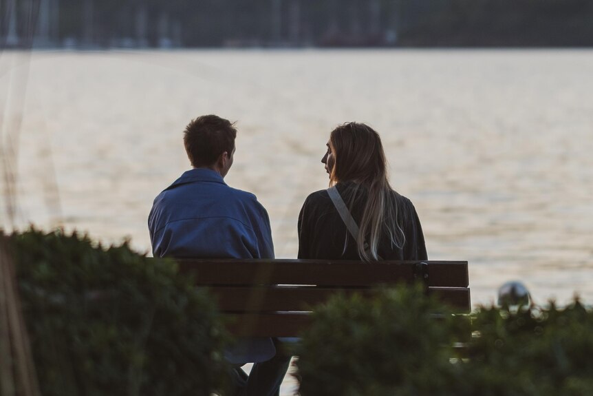 Man and woman sitting on bench talking in the distance