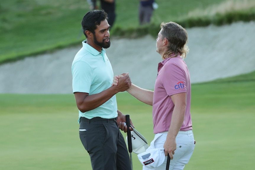 Tony Finau and Cam Smith loko each other in the eye and shake hands on the 18th green