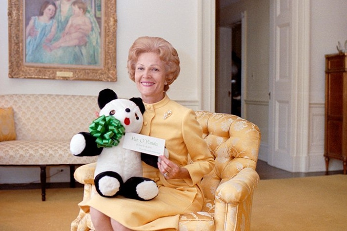 一位坐着的女人拿着一只玩具熊猫的旧照片。