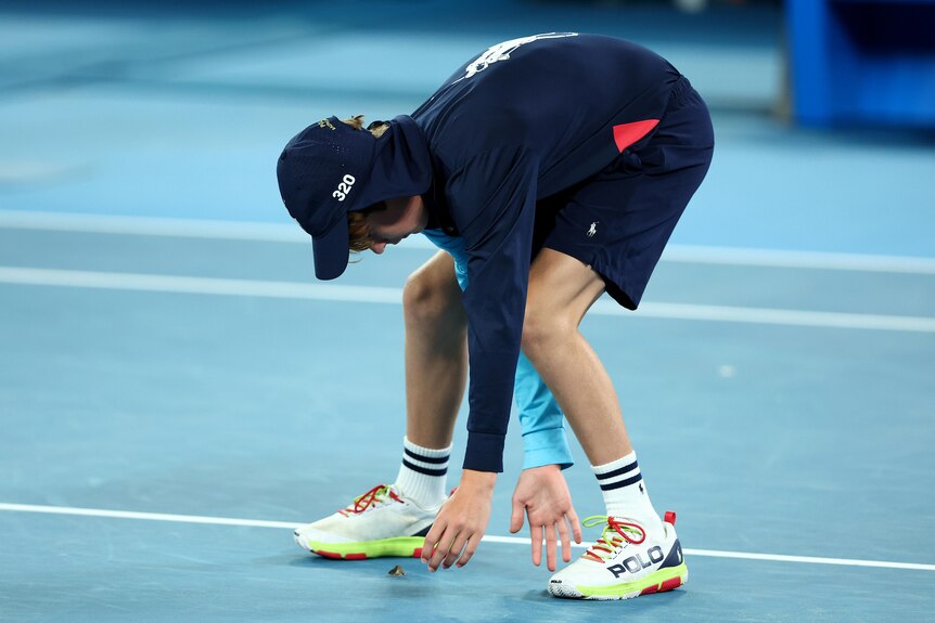 A ball kid bends over to try to catch a moth during an Australian Open match.