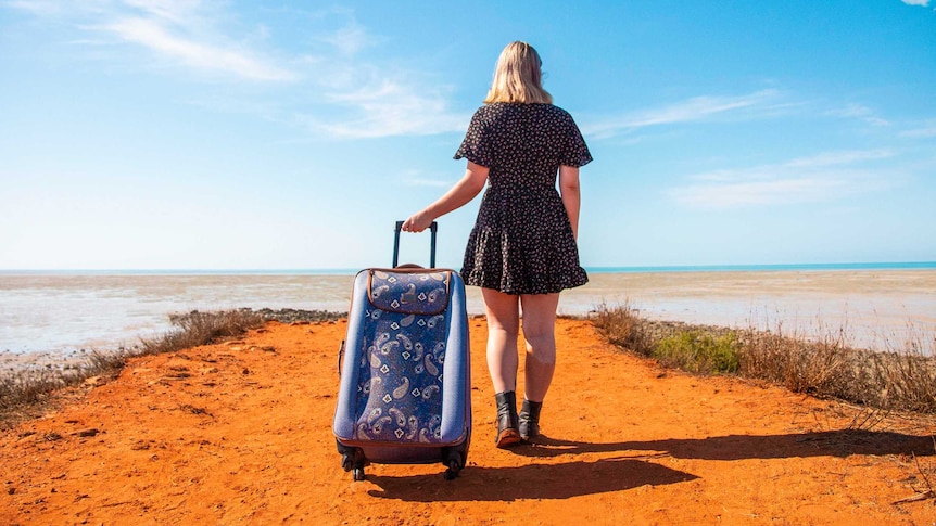 A girl stands holding a suitcase at the end of the groyne at Town Beach in Broome looking out to the ocean