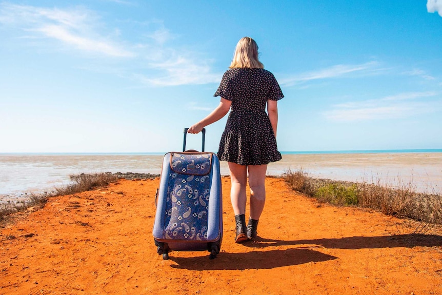 A woman drags a suitcase through the red dirt of outback WA.