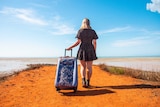 A girl stands holding a suitcase at the end of the groyne at Town Beach in Broome looking out to the ocean