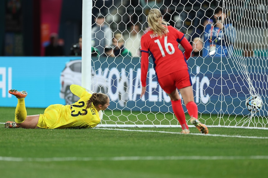 A goalkeeper lies on the ground after diving full-length in vain to try and stop a ball bulging the back of the net.