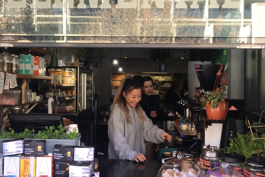 Two people stand behind a coffee shop counter laughing, surrounded by packets of coffee beans.