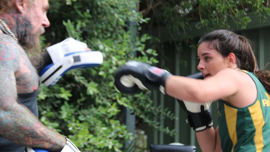 A female boxer spars outdoors with a heavily tattooed man