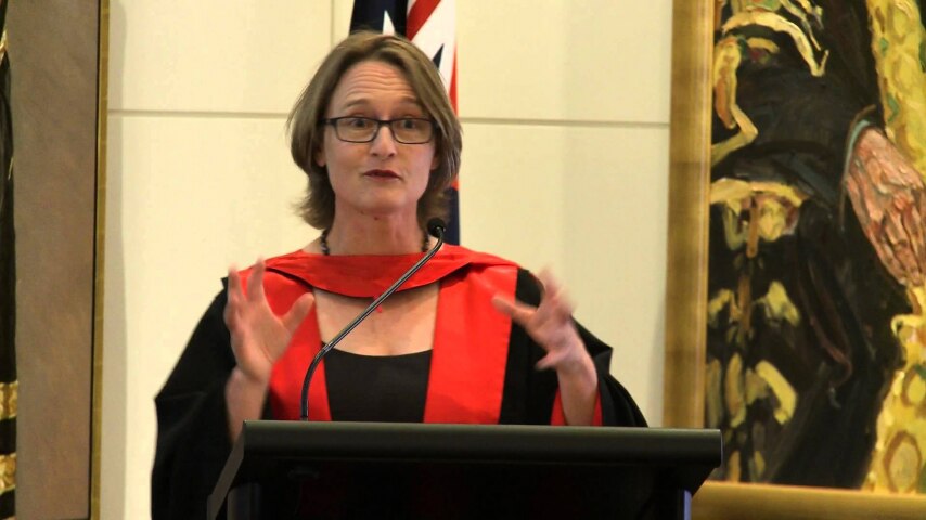 一名穿着教授袍的白人女性在讲台上发表演讲