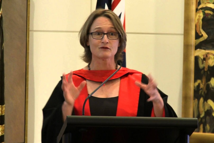 A woman wearing regalia is giving speech on the stage. 