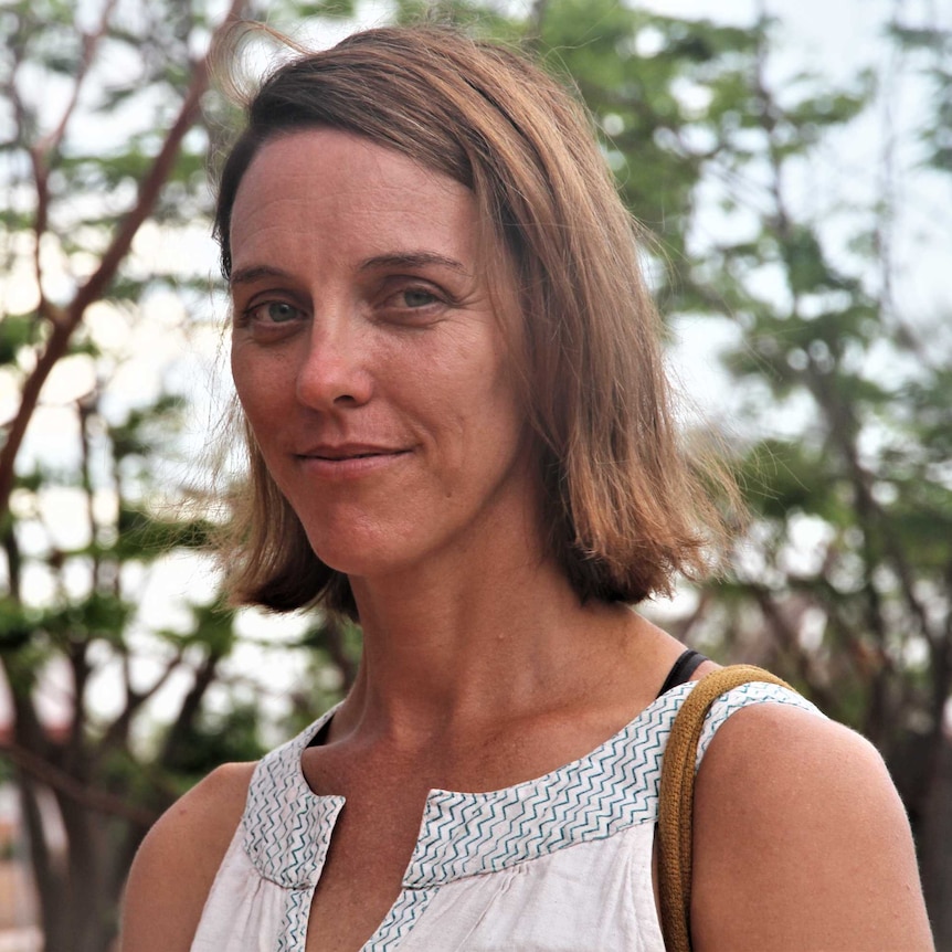 A woman stands in front of a tree.