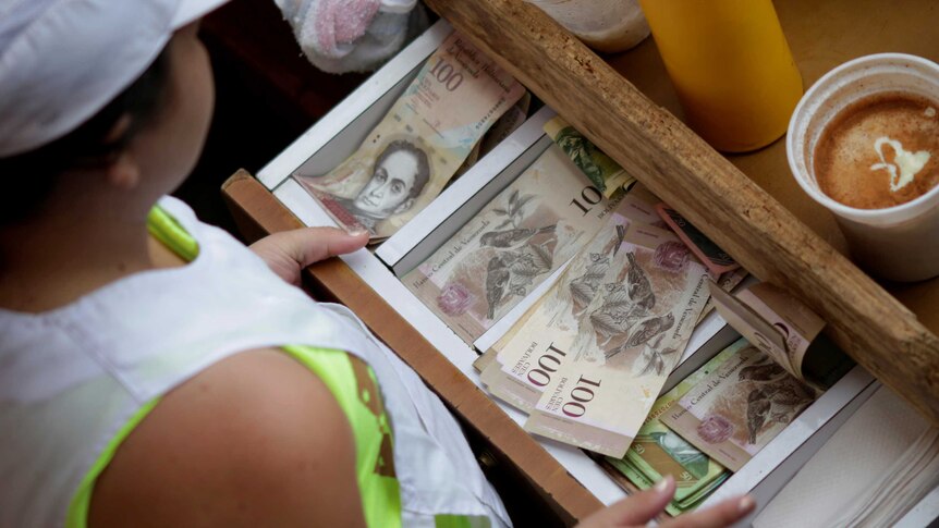 A cashier receives Venezuelan bolivar notes at a market in downtown Caracas, Venezuela, December 7, 2016