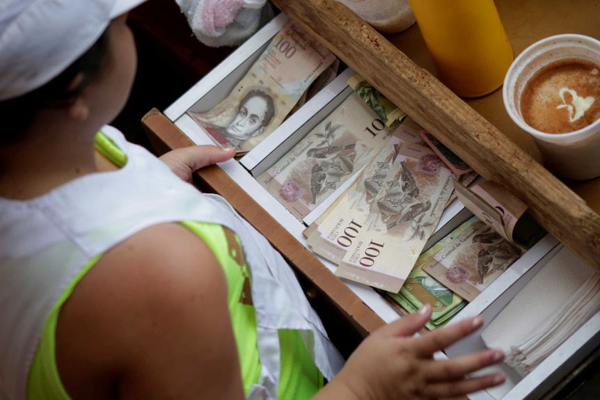 A cashier receives Venezuelan bolivar notes at a market in downtown Caracas, Venezuela, December 7, 2016