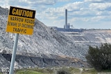 A sign saying "caution" in front of an open pit coal mine and power station.