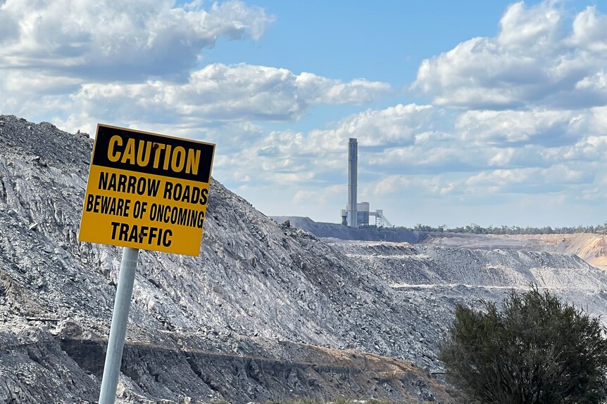 Photo d'un panneau indiquant la prudence avec une mine de charbon à ciel ouvert et une centrale électrique en arrière-plan