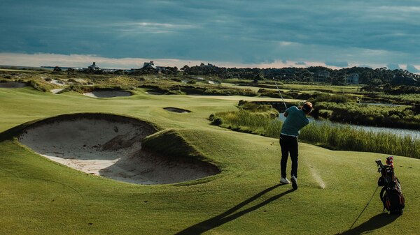 A golfer tees off into a vast expanse of greens.