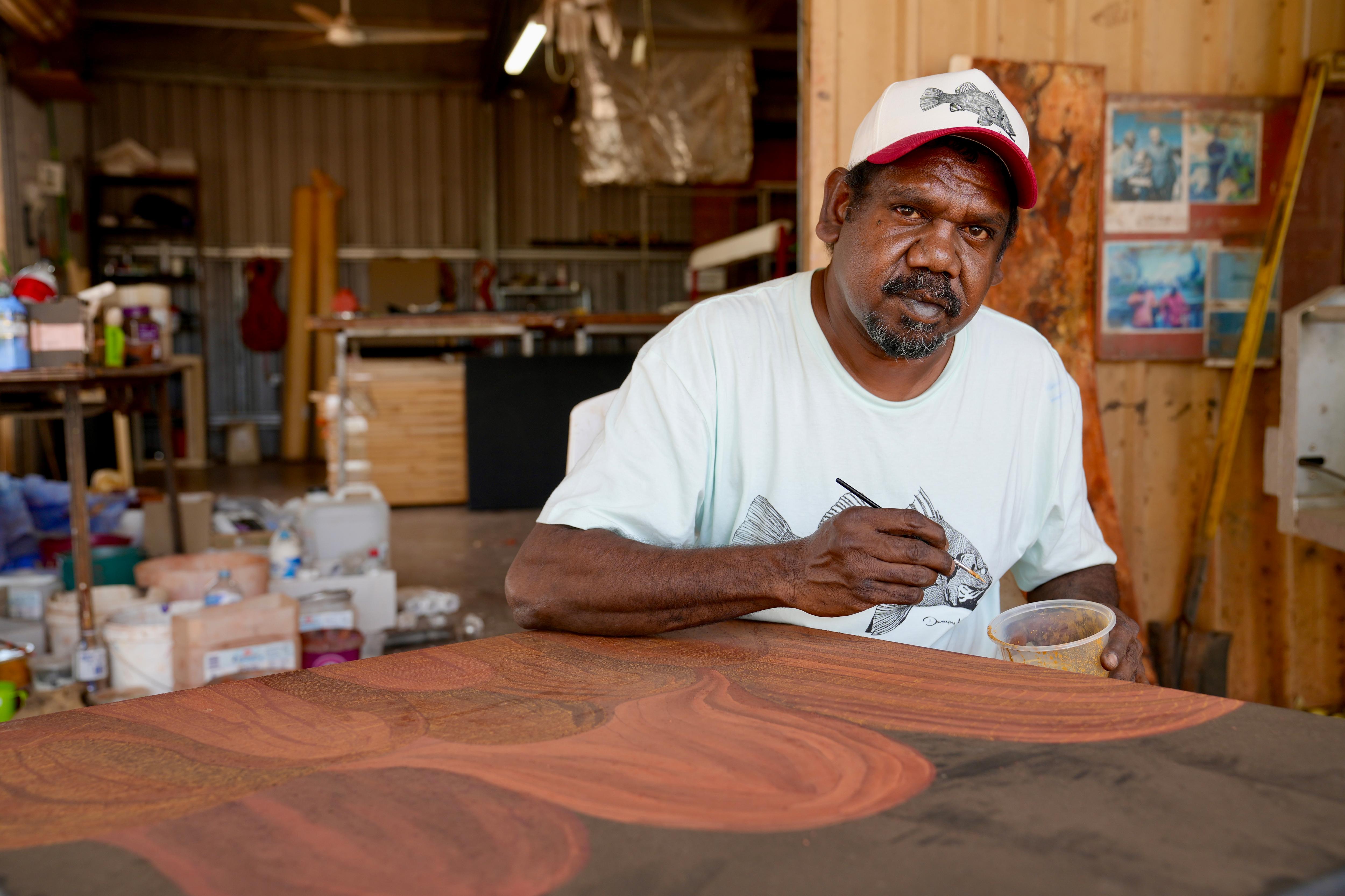 Aboriginal man with t-shirt and cap painting red hills
