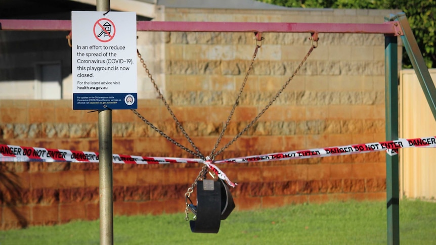 A sign warning people of coronavirus sits in front of a swing set taped off