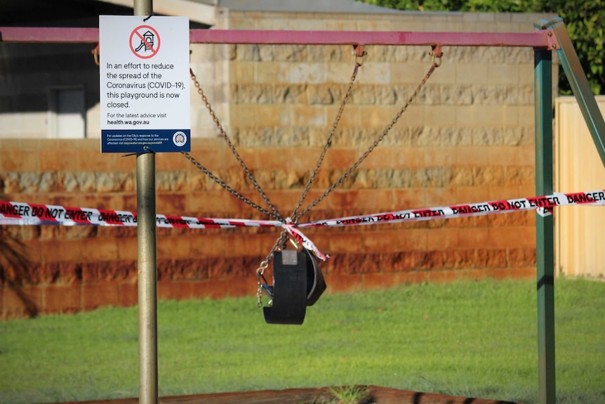 A sign warning people of coronavirus sits in front of a swing set taped off