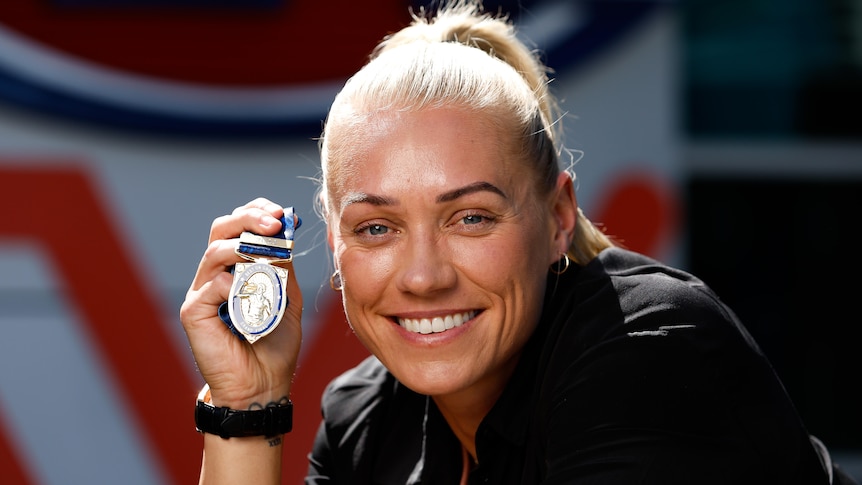 Erin Phillips smiles while holding up a small medal