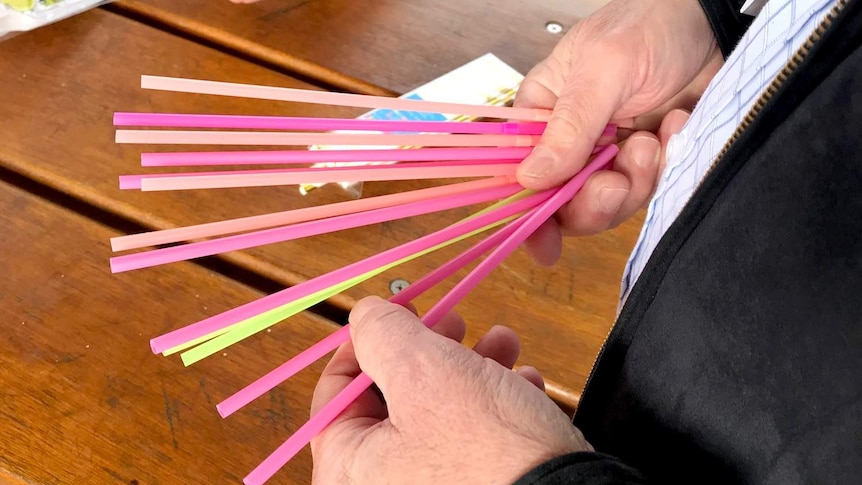 A hand holds several plastic straws.