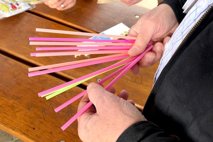 A hand holds several plastic straws.