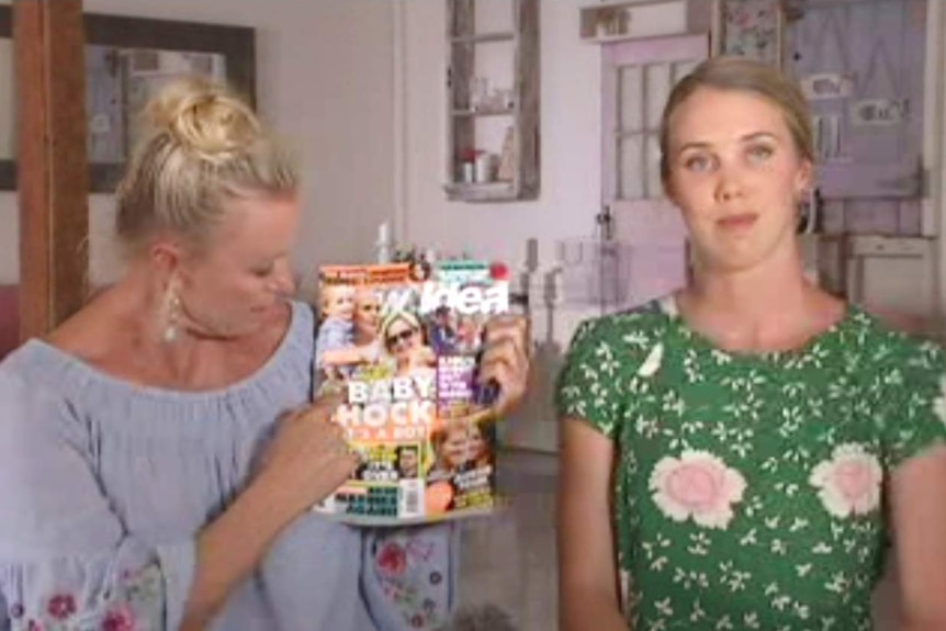 Two women, one holding a magazine and looking at it and another looking at the camera.