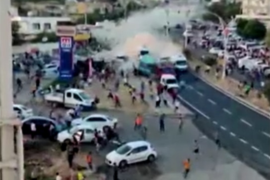 Une capture d'écran d'une vidéo montre un camion vert fonçant dans une foule de personnes.  Il y a de la fumée grise derrière le camion sur la route. 
