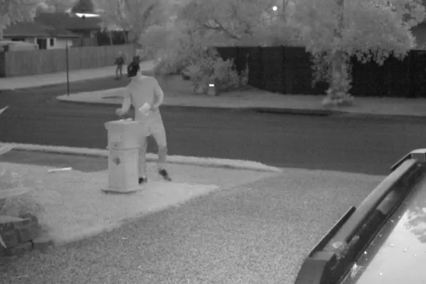 A black and white CCTV still shows a person in a black cap putting hate mail in a home's letter box