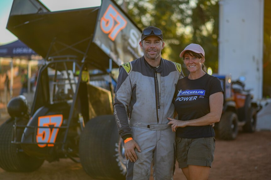 A man and woman, arm in arm, in front of a sprint car