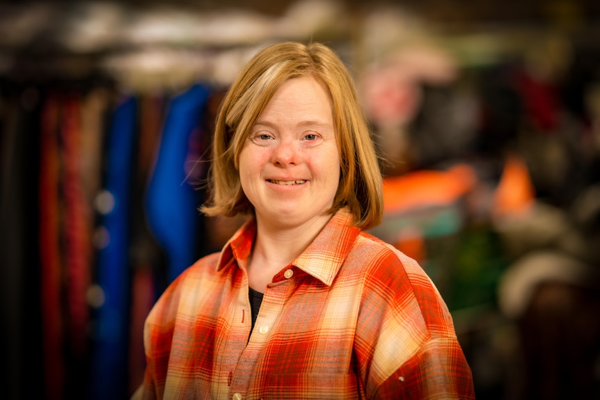 A young woman with a blonde bob haircut dressed in a check shirt grins at the camera