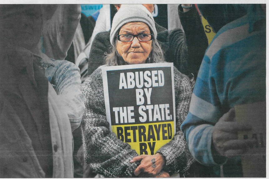 A woman holds up a sign at the WA Redress rally saying "Abused by the State"