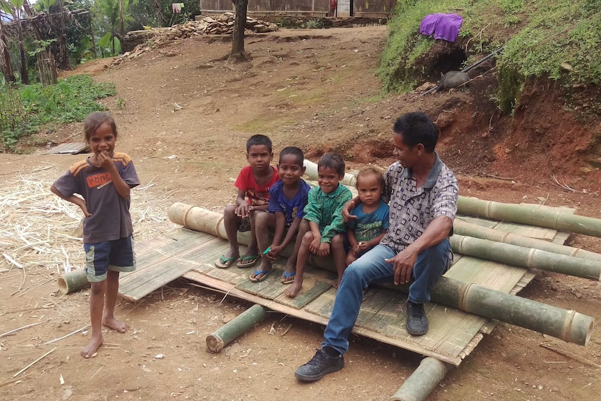 A man sitting with five young children in a regional village.