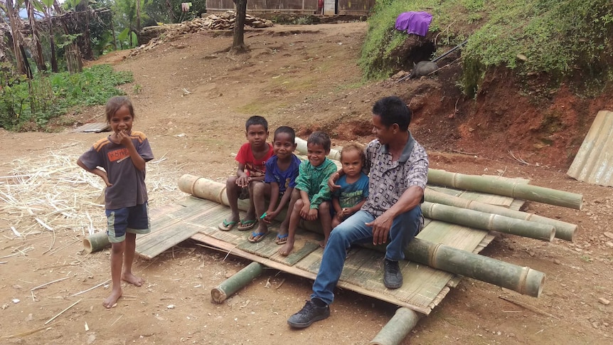 A man sitting with five young children in a regional village.