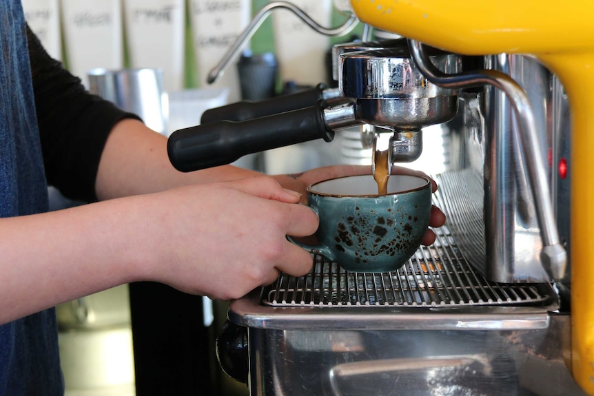 A person holds a turquoise coffee mug underneath the spout of an espresso machine