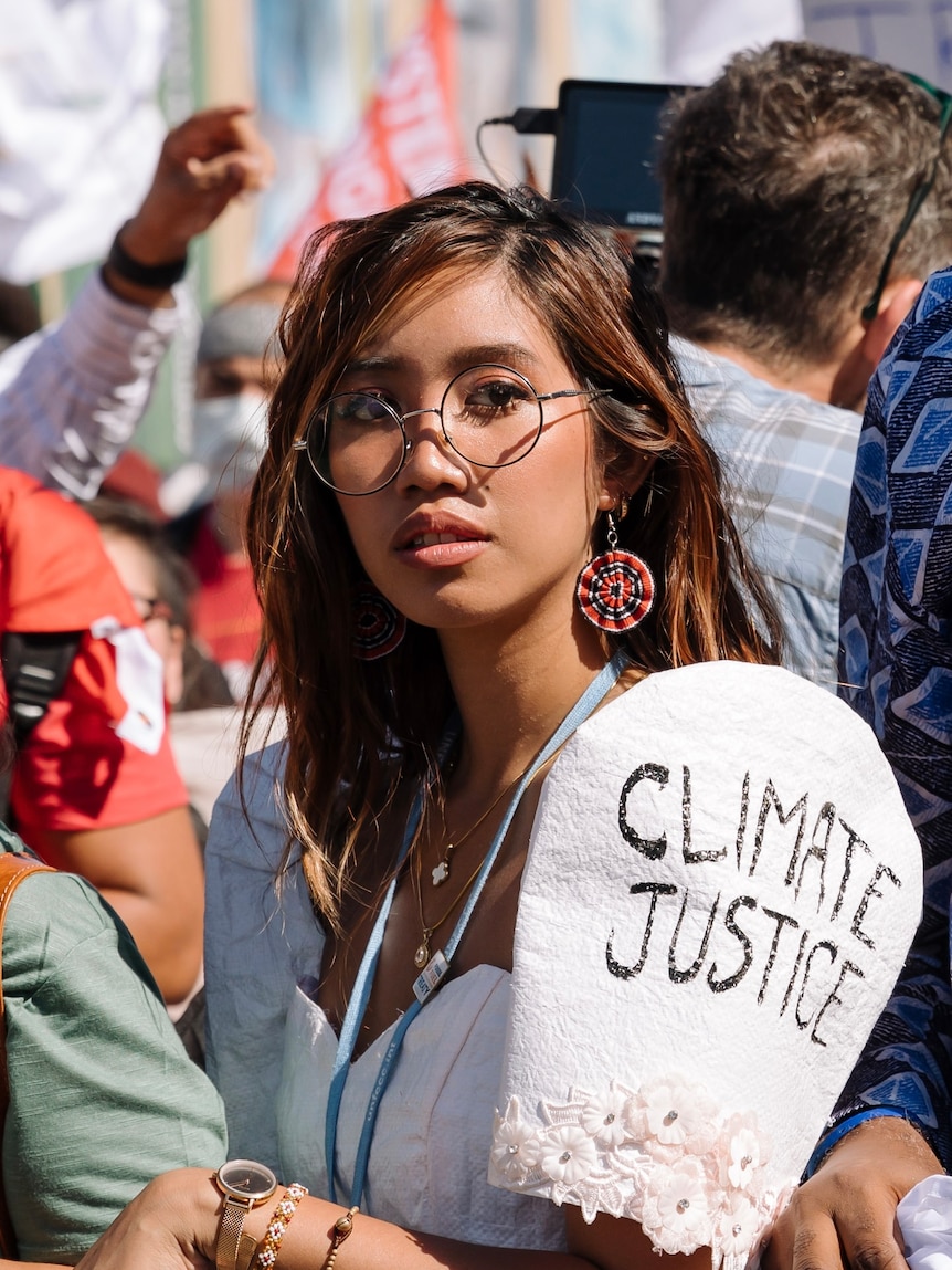 young woman wearing glasses and a top with the words "climate justice" on visible on her sleeve