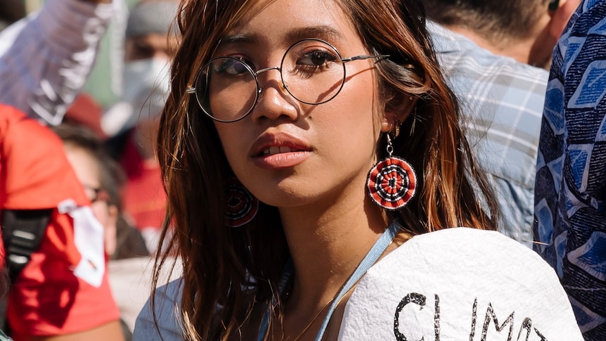 young woman wearing glasses and a top with the words "climate justice" on visible on her sleeve